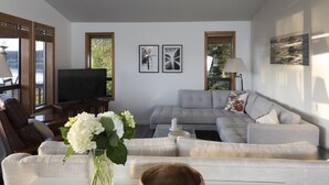 A modern living room with a grey sectional sofa, a wooden coffee table, a TV, and a vase with white flowers. - South Whidbey with water view, beach and hiking  (Clinton)
