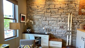 A modern room with a stone wall, a desk with a lamp, a chair, a sofa, and a ski rack. - Downtown MainStreet Penthouse 1BR five star Rental with parking overlooking main (Durango)