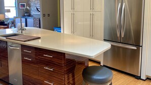 A modern kitchen with a stainless steel refrigerator, wooden cabinetry, and a central island with a sink and countertop. - Downtown MainStreet Penthouse 1BR five star Rental with parking overlooking main (Durango)