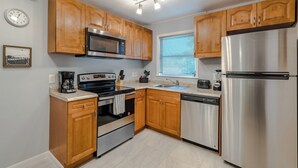A modern kitchen with wooden cabinets, stainless steel appliances, and a window with blinds.