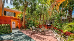 A patio with a table and chairs, surrounded by lush greenery and palm trees.