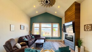 A spacious living room with a high ceiling, a fireplace, and large windows. - Roof Top Deck-Hot Tub-Steam Shower-Arcade Games-4car Garage-Chef`s Kitchen (Spearfish)