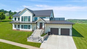 A modern two-story house with a large garage, a well-maintained lawn, and a clear sky. - Roof Top Deck-Hot Tub-Steam Shower-Arcade Games-4car Garage-Chef`s Kitchen (Spearfish)