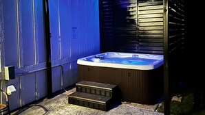 A hot tub under a covered area with steps leading up to it, surrounded by a concrete patio. - Roof Top Deck-Hot Tub-Steam Shower-Arcade Games-4car Garage-Chef`s Kitchen (Spearfish)