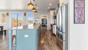 A modern kitchen with a central island, stainless steel appliances, pendant lighting, and a view of the outdoors. - Roof Top Deck-Hot Tub-Steam Shower-Arcade Games-4car Garage-Chef`s Kitchen (Spearfish)
