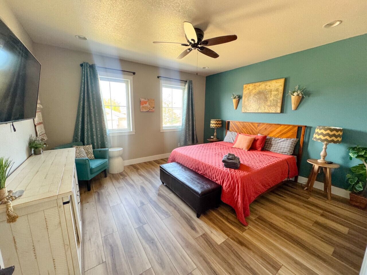 A bedroom with a bed, a desk, a chair, a ceiling fan, and a window.