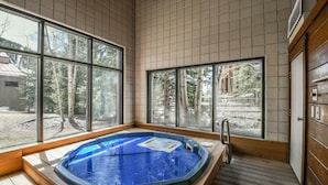A hot tub in a room with large windows, wooden flooring, and a view of trees and a building outside. - Family-Friendly Escape | Balcony & Scenic Views (Keystone)