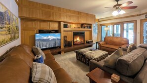 Una sala de estar acogedora con chimenea, sofás de cuero, televisor y ventilador de techo.