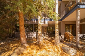 A multi-story building with a covered outdoor area featuring trees, a patio, and a stack of firewood.