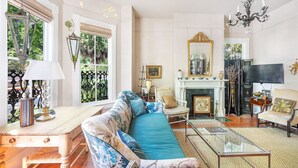 A living room with a sofa, chairs, a fireplace, a television, and a chandelier. - Bright, Historic Row Home Minutes from Forsyth by Lucky Savannah (Savannah)