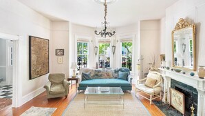 A spacious living room with a teal sofa, a glass coffee table, and a fireplace. - Bright, Historic Row Home Minutes from Forsyth by Lucky Savannah (Savannah)
