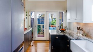 A kitchen with a refrigerator, cabinets, a countertop with a bowl of fruit, and a door leading to a balcony. - Bright, Historic Row Home Minutes from Forsyth by Lucky Savannah (Savannah)
