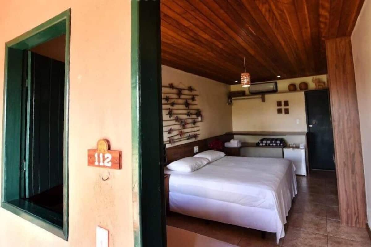 Una habitación con dos camas, techo de madera, estante empotrado con objetos decorativos y una pequeña cocina.