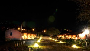 Une vue nocturne d’un hôtel avec plusieurs bâtiments illuminés, un chemin bien éclairé et une végétation luxuriante environnante.