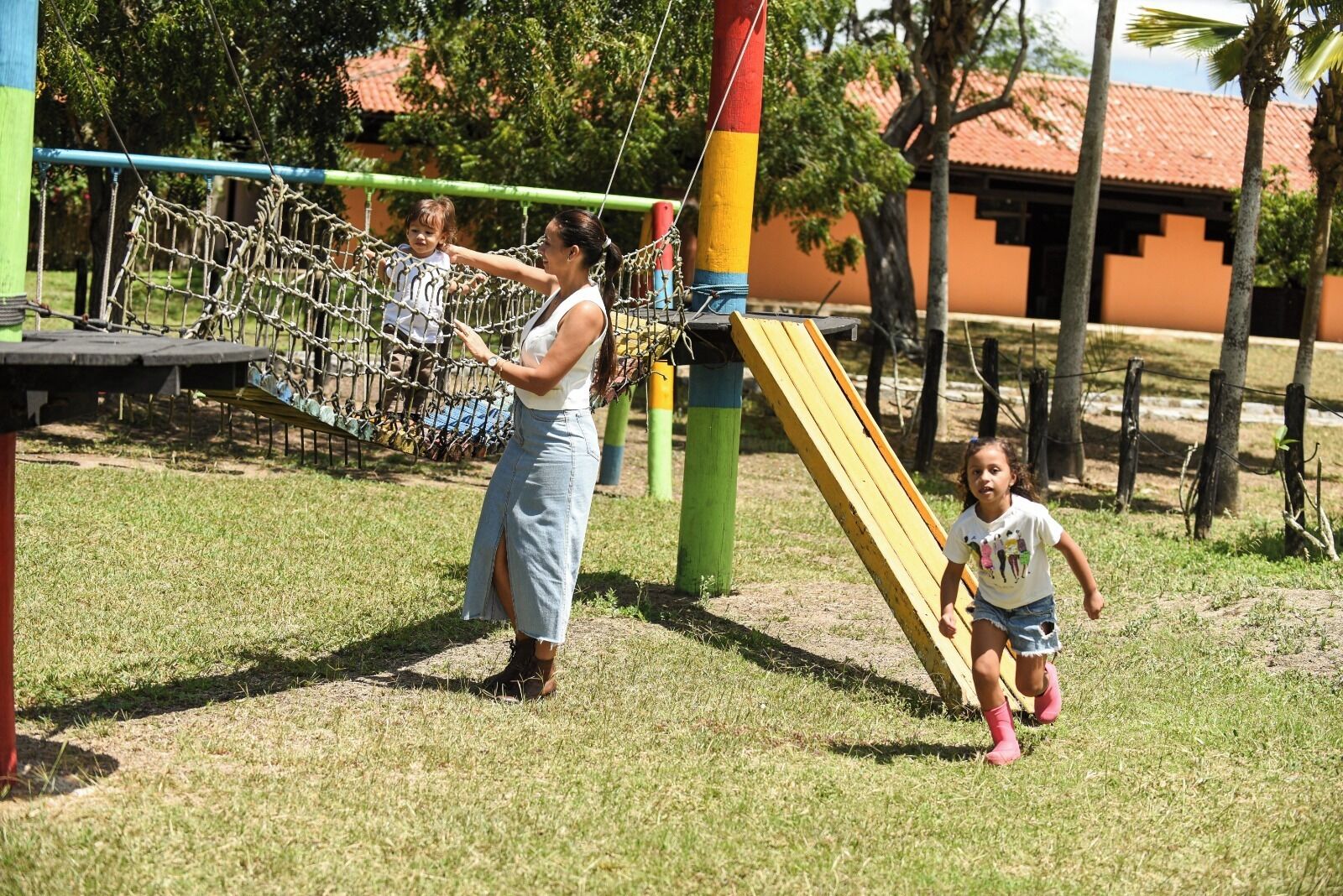 Um parquinho com uma ponte de corda, um escorrega e uma estrutura de escalada.