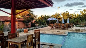 Un espace aménagé au bord de la piscine, comprenant un coin salon couvert, des chaises longues et des parasols.