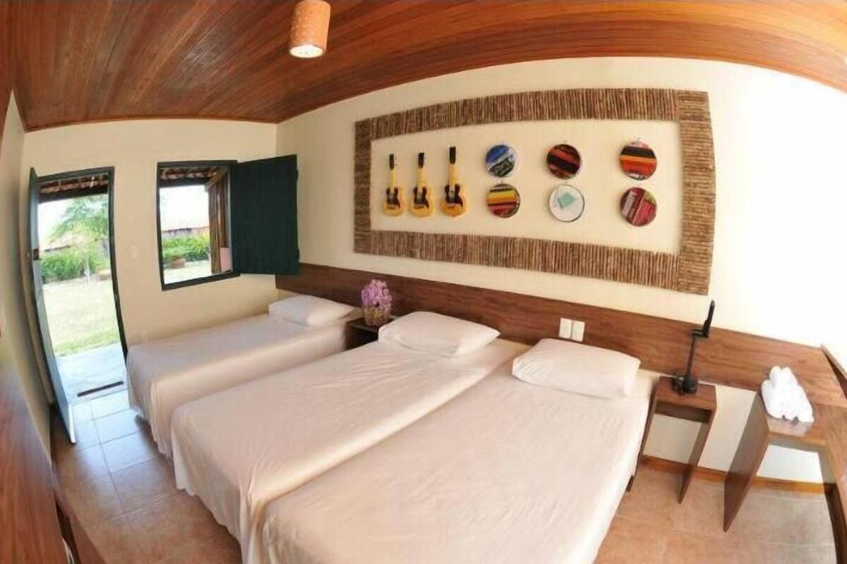 Habitación de hotel con dos camas, techo de madera, pared decorada con placas y ventana con cortinas.