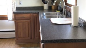 A kitchen with wooden cabinets, a granite countertop, a sink, and a mat on the floor. - Heart of the Seneca Lake Wine Trail (Burdett)