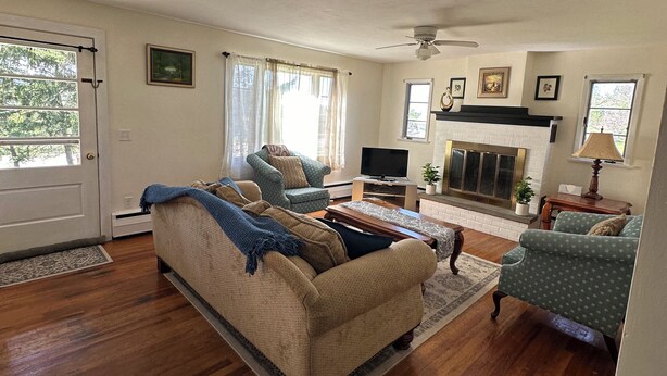 A living room with a beige sofa, a patterned armchair, a television, a fireplace, and a ceiling fan. - Heart of the Seneca Lake Wine Trail (Burdett)