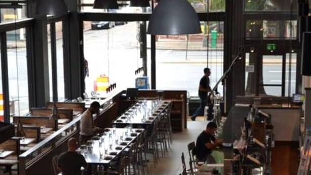 Un restaurante espacioso con techos altos, ventanas amplias y una zona de bar central.