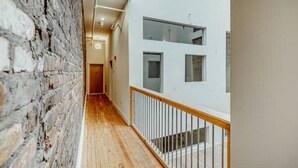 A narrow hallway with a wooden floor, white walls, and a brick wall on one side.