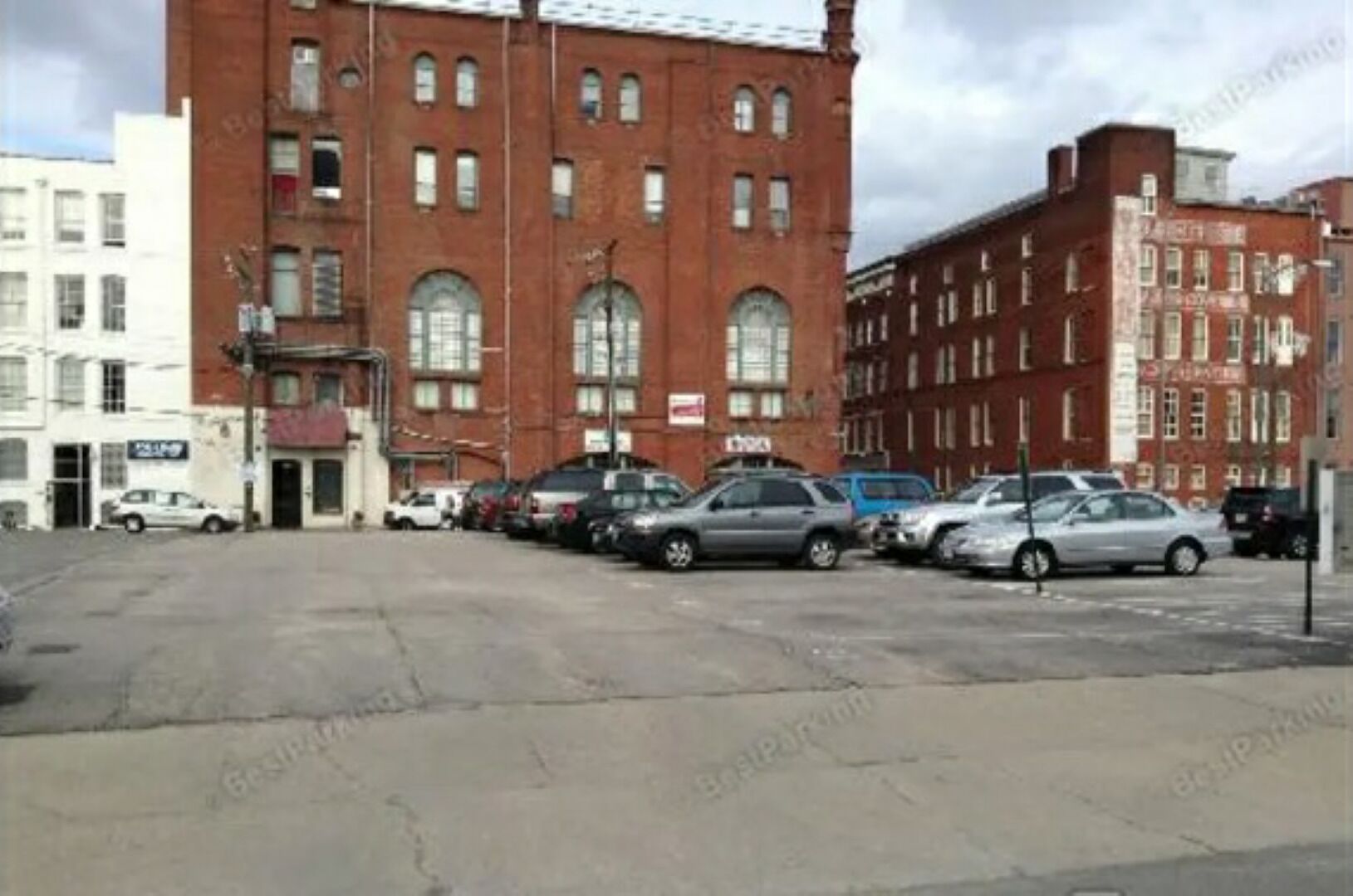 A parking lot with several cars parked in front of a red brick building with multiple windows and a sign that reads "Coca-Cola."