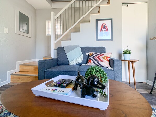 Ein modernes Wohnzimmer mit einem grauen Sofa, einem Couchtisch mit einer Auflage und einer Treppe sowie einer Tür mit einem gerahmten Bild.