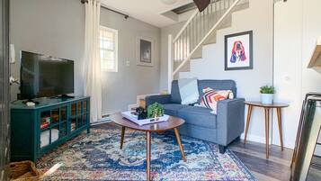 Un salon avec un canapé, une table basse, un téléviseur et un escalier.