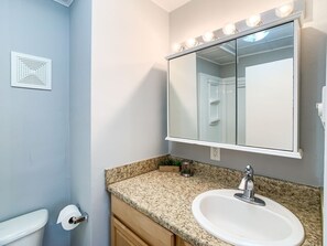 Ein Badezimmer mit einem weißen Waschbecken, einer Granit-Arbeitsplatte und einem Spiegel mit Beleuchtung.