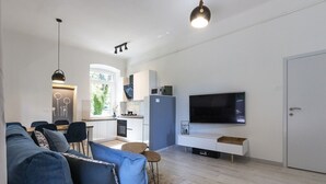 En moderne stue med sofa, fjernsyn og et køkkenområde.