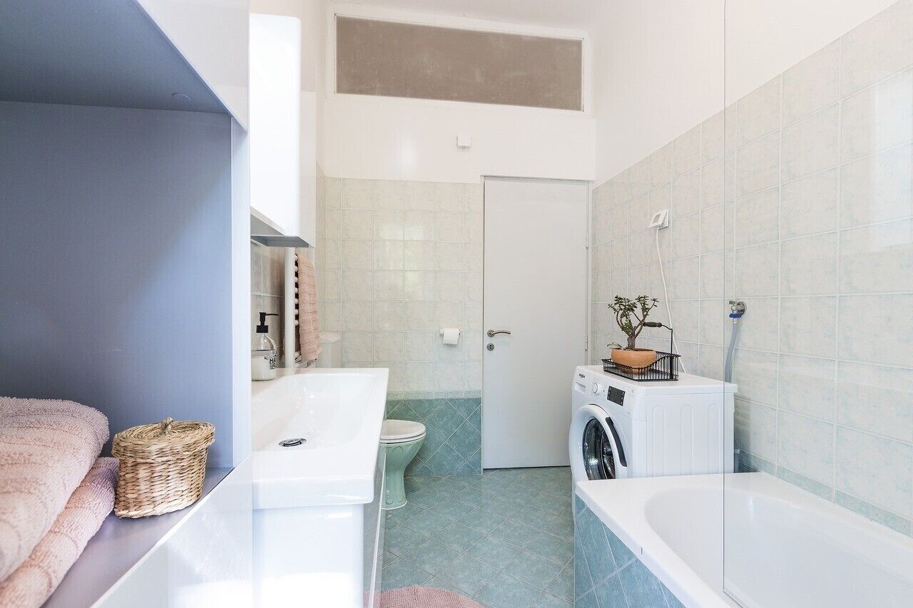 A compact bathroom with a white sink, a toilet, a washing machine, and a bathtub.