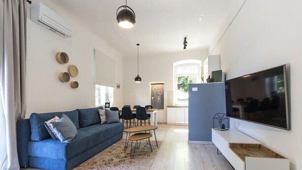 En moderne stue med en blå sofa, et spisebord med stole, et fjernsyn på væggen og en aircondition.