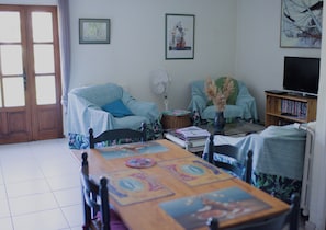 A living room with a wooden table, two chairs, a sofa, a television, and a bookshelf.