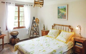 A bedroom with a bed, a window, a radiator, a wooden ladder, a painting, and a lamp.