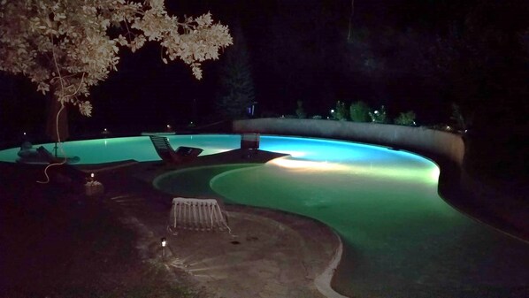 A swimming pool with a curved edge, surrounded by lounge chairs and a small table.