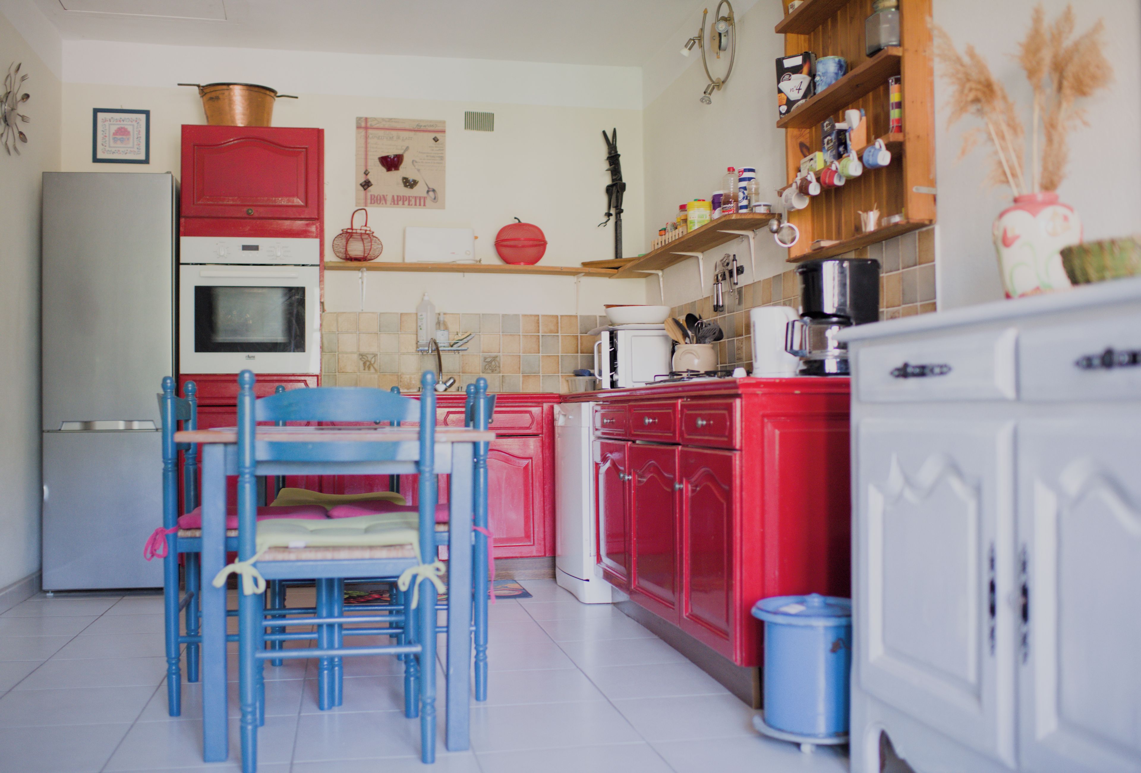 Cozinha com armários vermelhos, geladeira branca e uma cadeira azul.