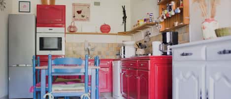 A kitchen with red cabinets, a white refrigerator, and a blue chair.