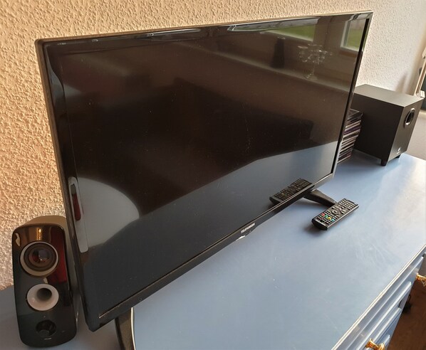 A flat-screen TV on a blue surface with a remote control and a speaker.