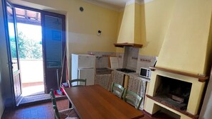 Un coin repas avec une table et des chaises en bois, une cuisine équipée d’une cuisinière et de placards, et une porte-fenêtre coulissante donnant sur un espace extérieur.