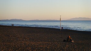 Une plage avec un mât de drapeau, des gens qui se promènent et des montagnes à l’horizon.
