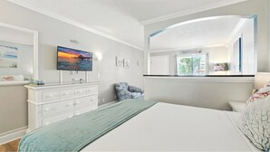 A bedroom with a bed, a dresser, a chair, a TV, and a window with a view.