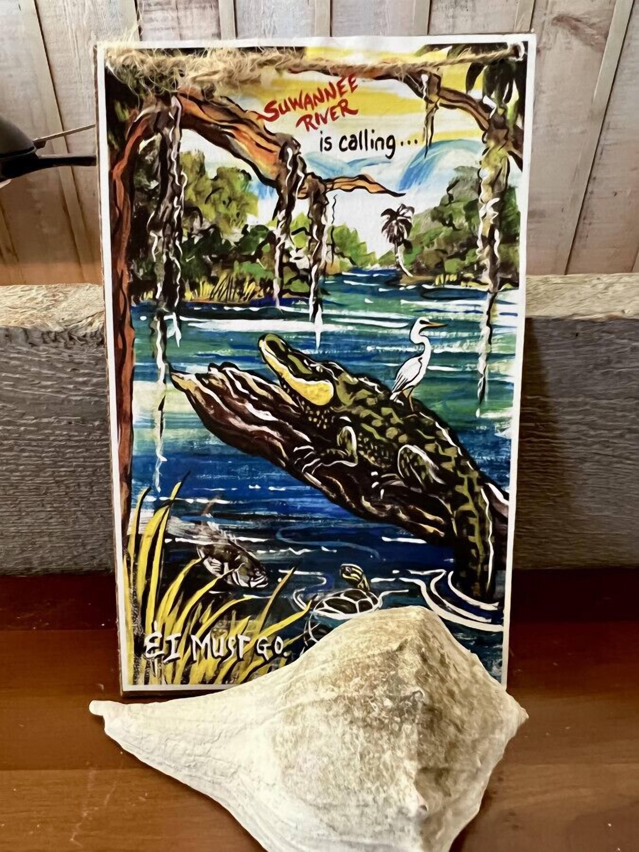 Une affiche représentant un crocodile et un oiseau, avec un texte sur la rivière Suwannee, et un petit tas de sable.