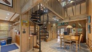A spacious room with a spiral staircase, wooden walls, a dining area, and a large window. - Hook, Wine & Sinker Cottage: Water Views, Kayaks, Bikes & Old Florida Charm (Cedar Key)