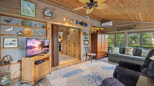 A cozy living room with a television, wicker furniture, and a ceiling fan. - Hook, Wine & Sinker Cottage: Water Views, Kayaks, Bikes & Old Florida Charm (Cedar Key)