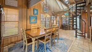 A wooden interior with a dining table, chairs, and a spiral staircase. - Hook, Wine & Sinker Cottage: Water Views, Kayaks, Bikes & Old Florida Charm (Cedar Key)