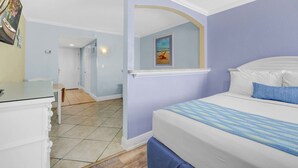 A bedroom with a bed, a desk, and a chair. There is a door leading to another room.