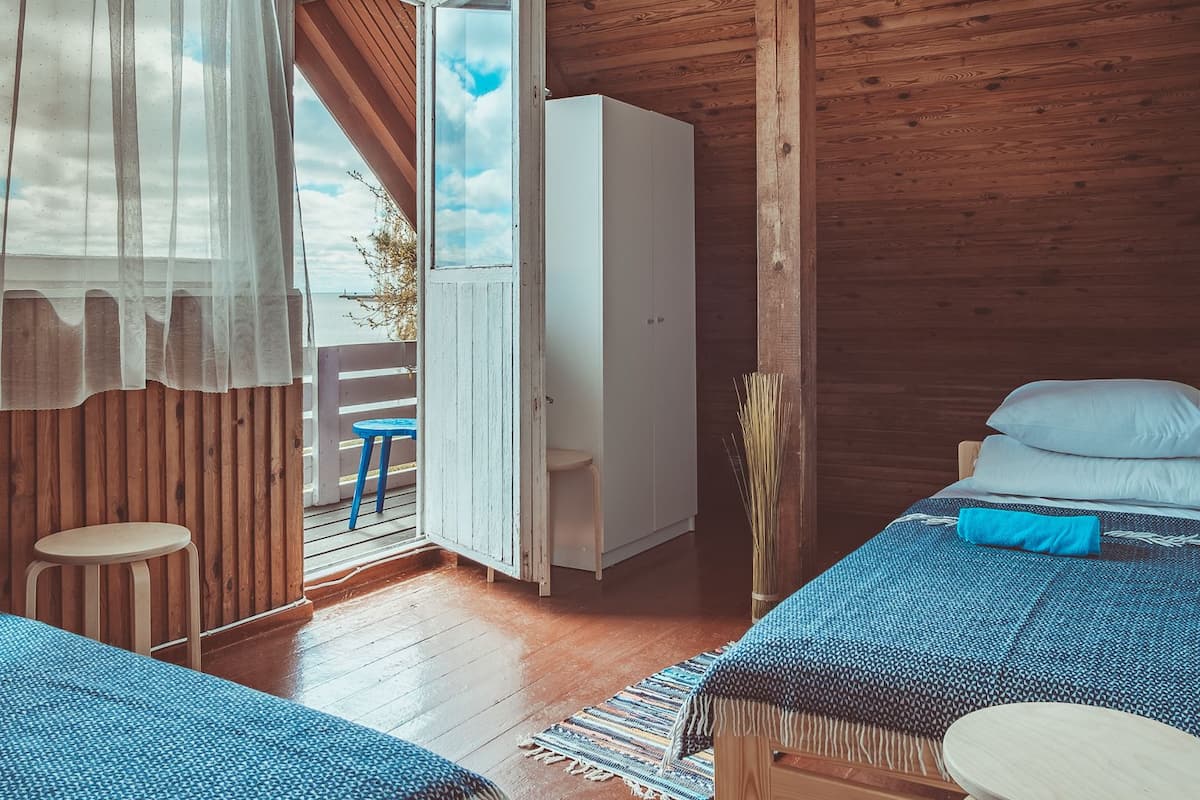 A cabin with wooden walls and ceiling, a bed with a blue blanket, a small table, and a wardrobe.