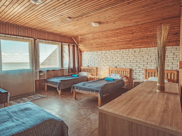 A cozy cabin-style room with two wooden beds, a brick wall, and a large window overlooking a beach.
