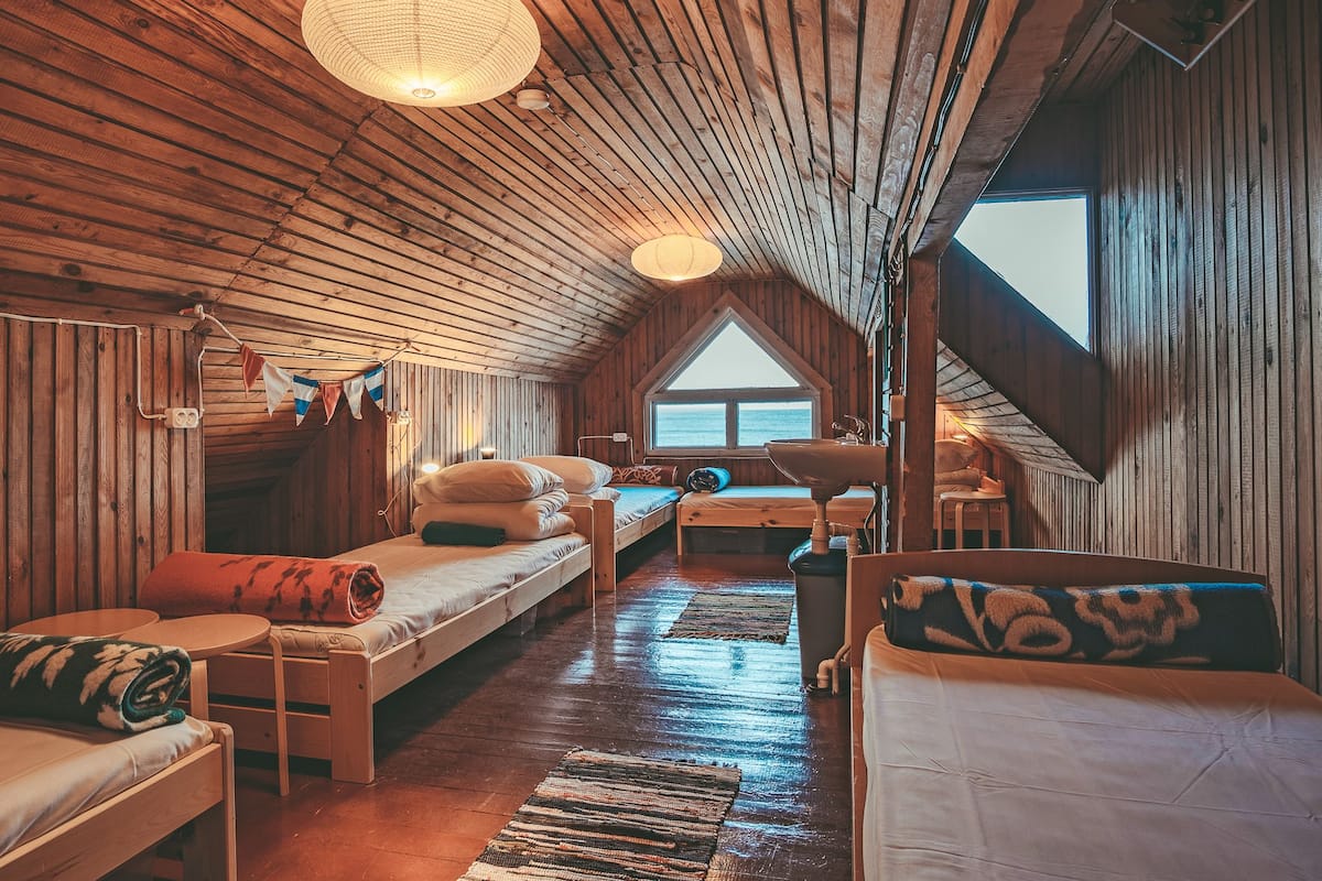 A cozy cabin with a wooden interior, a loft bed, a small table, and a view of the outdoors.