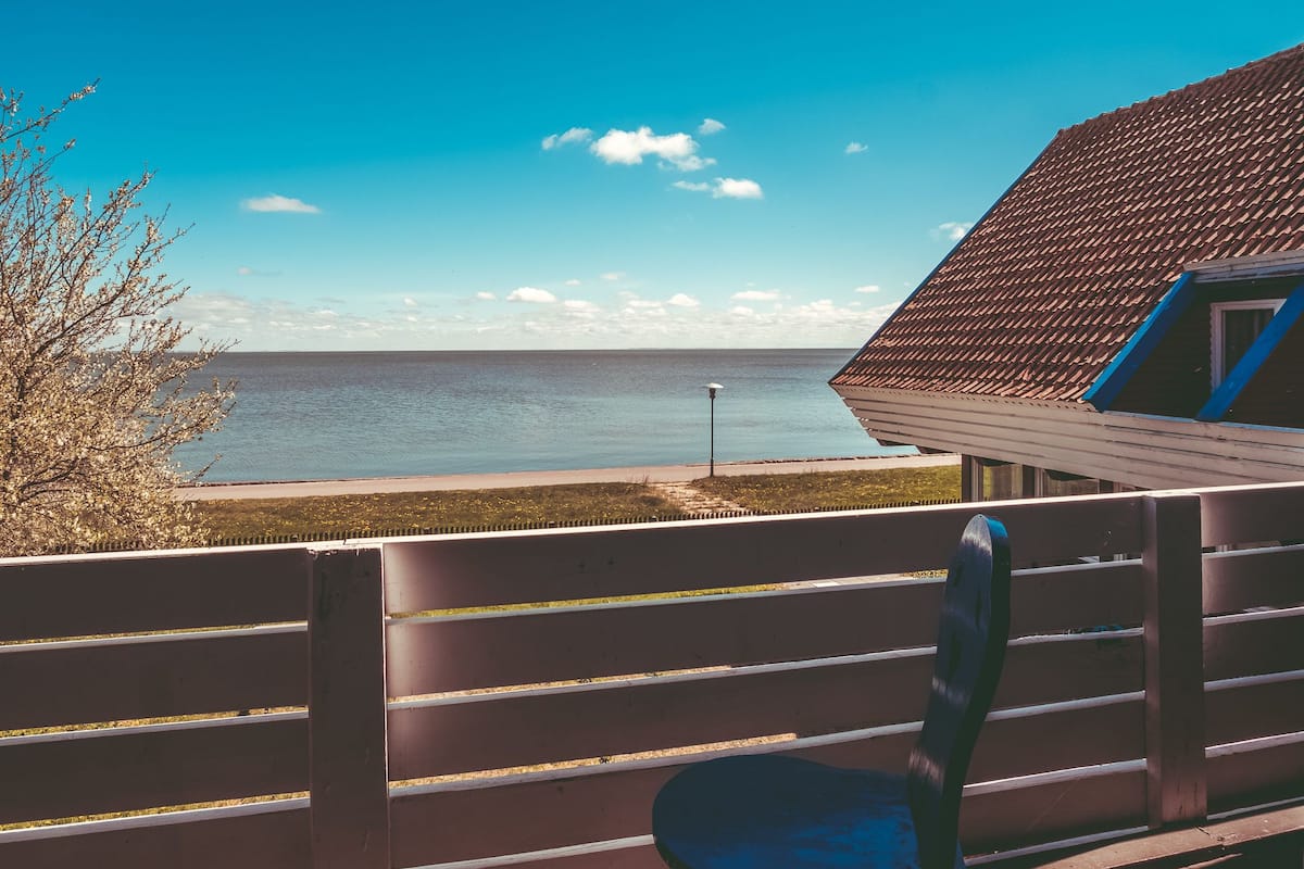A balcony with a view of the sea, a tiled roof, and a tree with white blossoms.